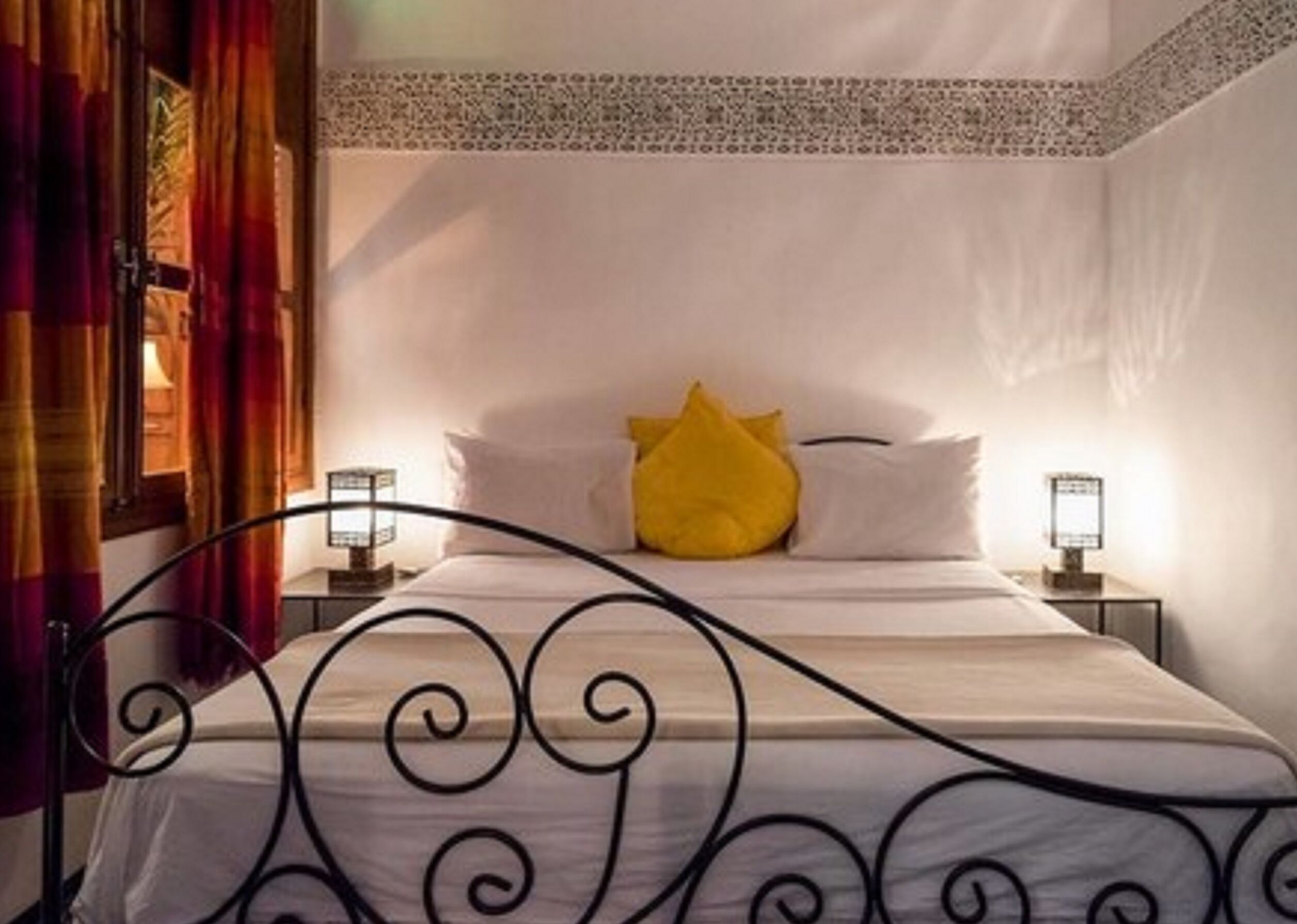Une chambre d’hôtel avec un lit, une table de chevet, une lampe et une fenêtre avec des rideaux.
