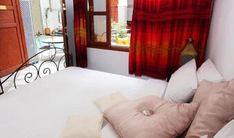 Quarto com cama, almofadas e janela com cortinas.