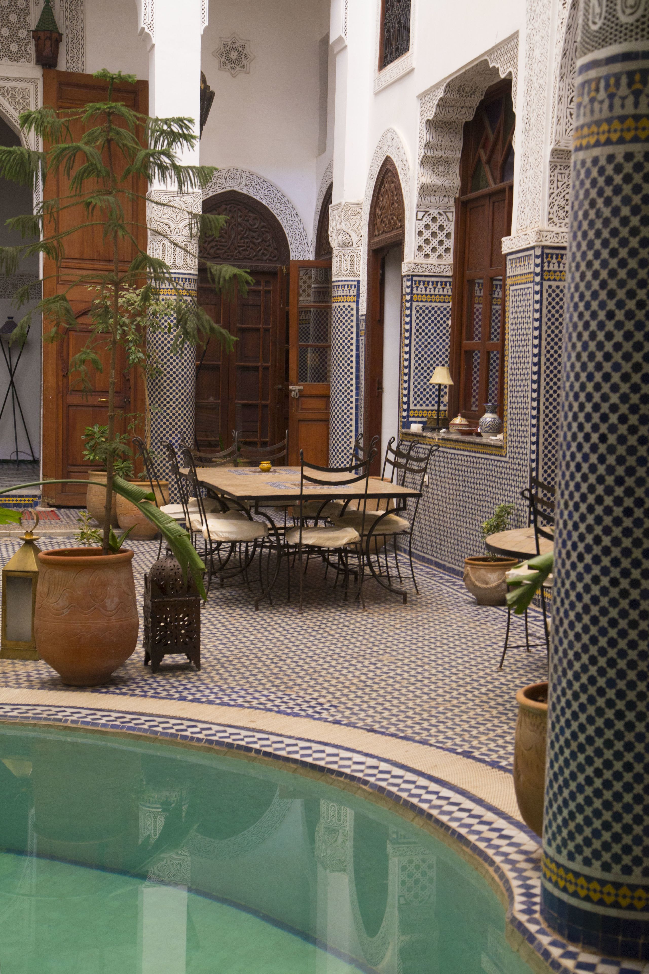 A courtyard with a pool, tiled floor, and a dining area with chairs and a table.
