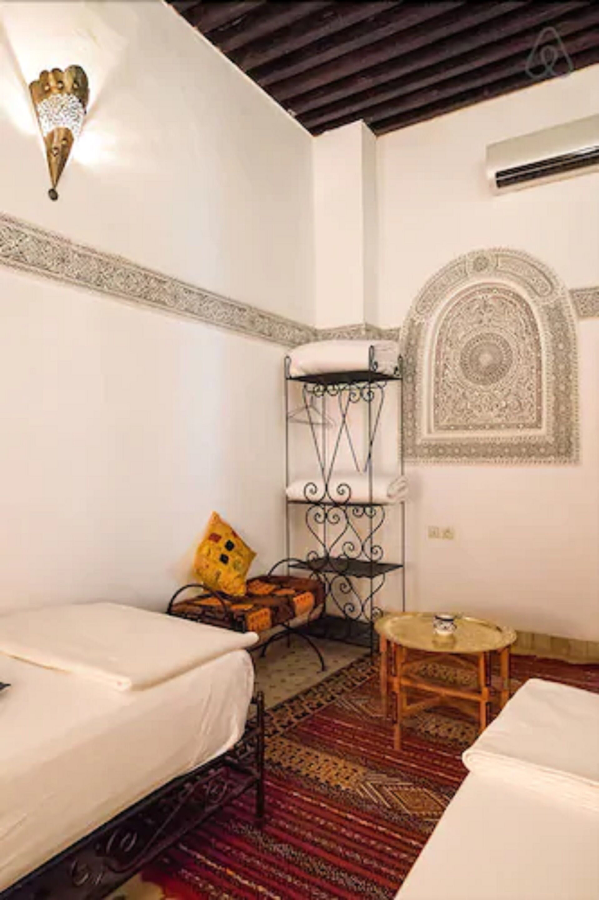 A room with two beds, a small table, a decorative wall piece, and a patterned rug.