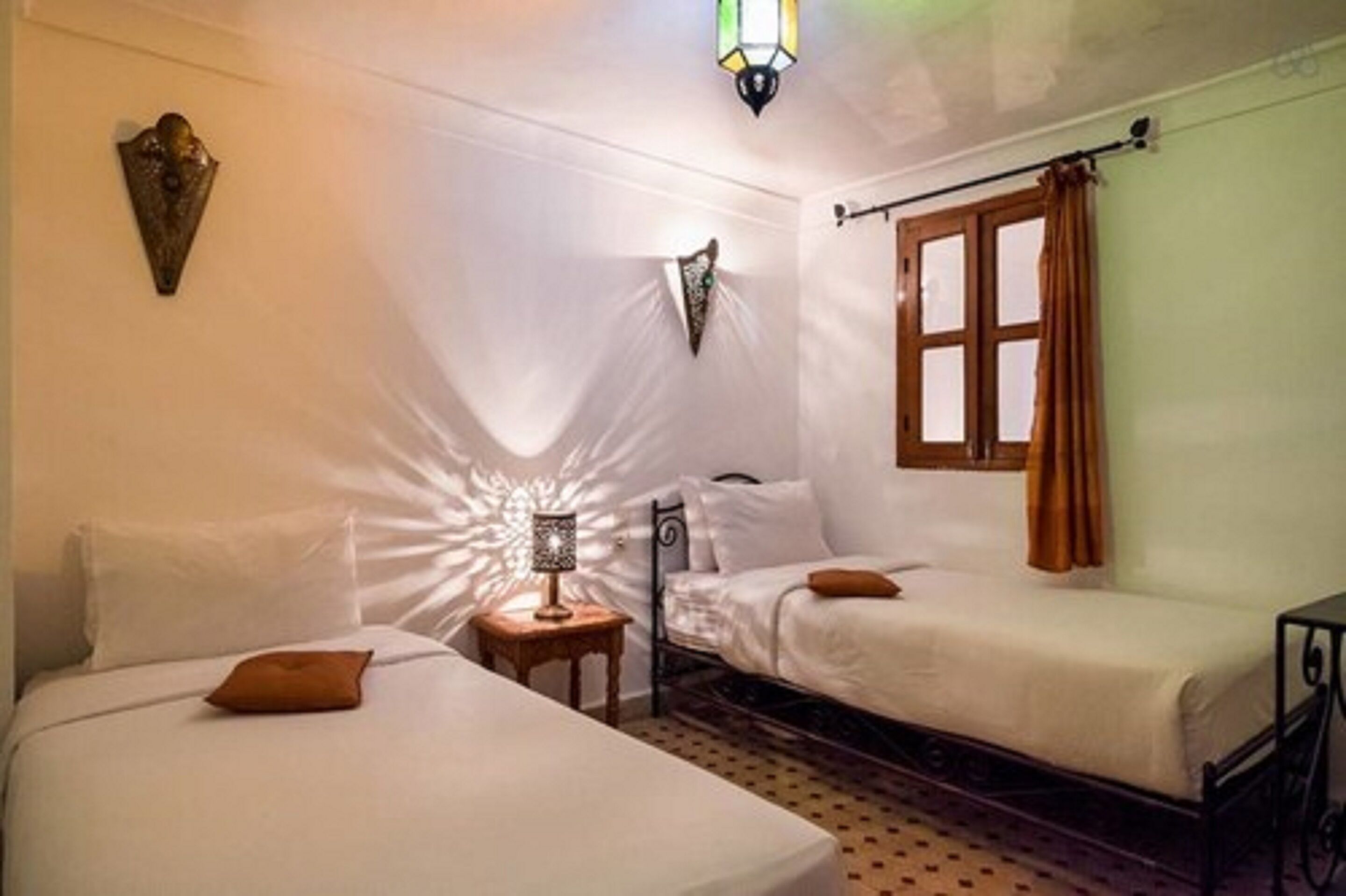 Una habitación con dos camas individuales, una mesita con lámpara y una ventana con cortinas.