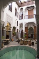 Un patio con piscina, plantas en macetas y mobiliario exterior.