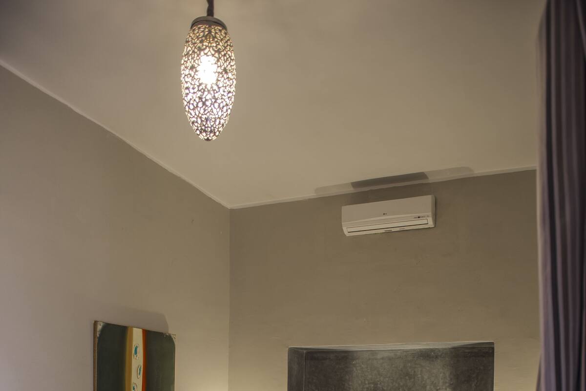 Quarto com cama grande, tapete estampado, luminária moderna e aparelho de ar condicionado.