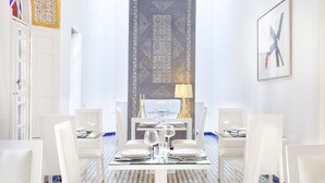 Un comedor con candelabro, alfombra estampada y mobiliario blanco.