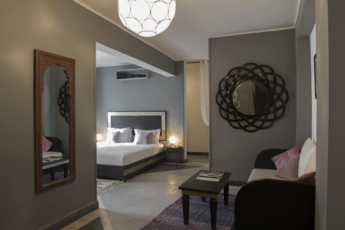 Quarto de hotel moderno com uma cama grande, área de estar com mesa de centro, espelho e decoração de parede única.
