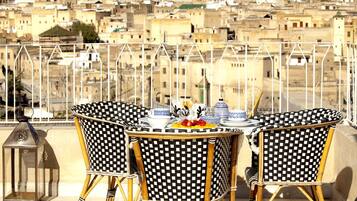 A terrace with two checkered wicker chairs, a table set with plates, bowls, and a lantern.
