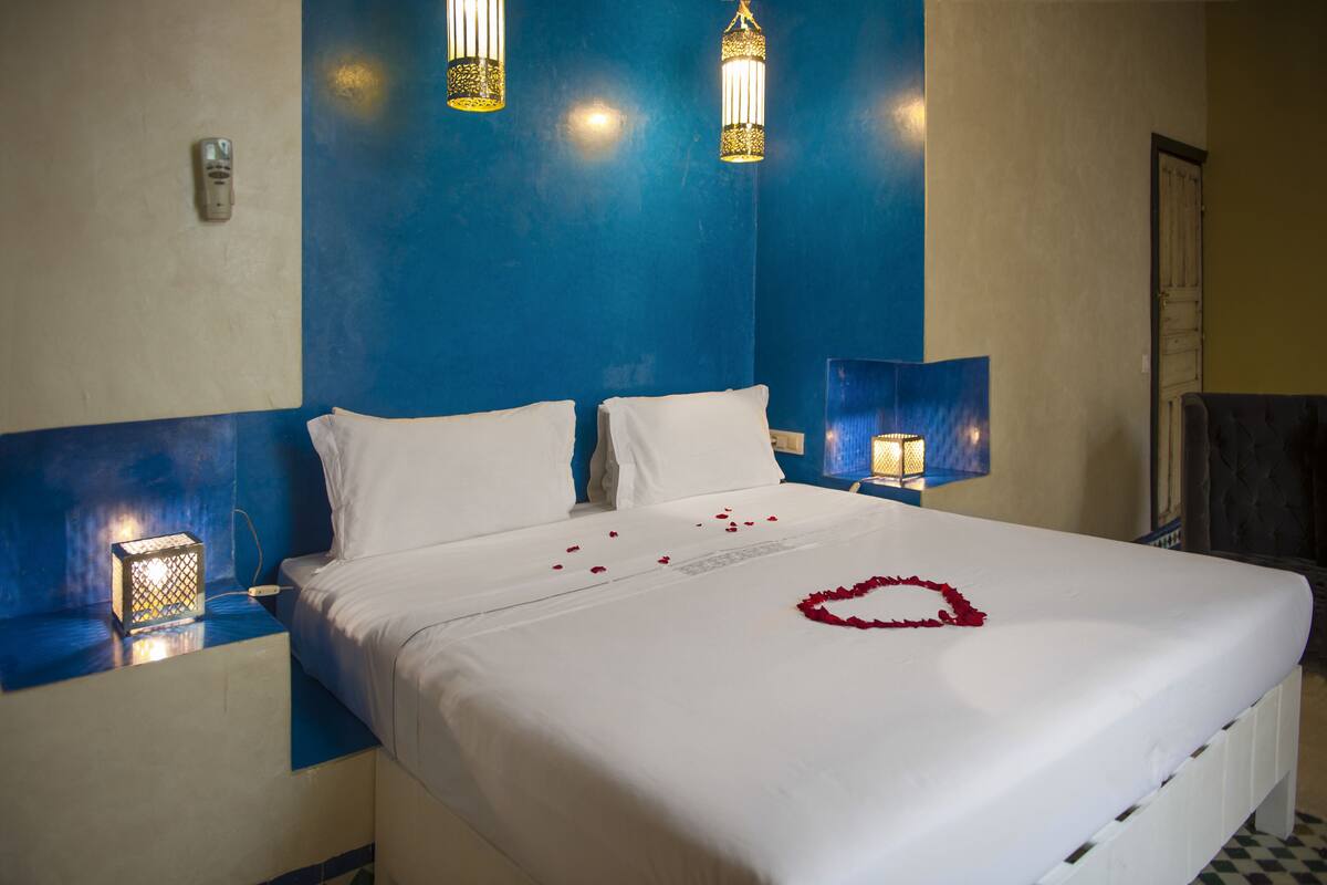 Cama bem arrumada com roupa de cama branca e uma decoração em formato de coração no edredom.