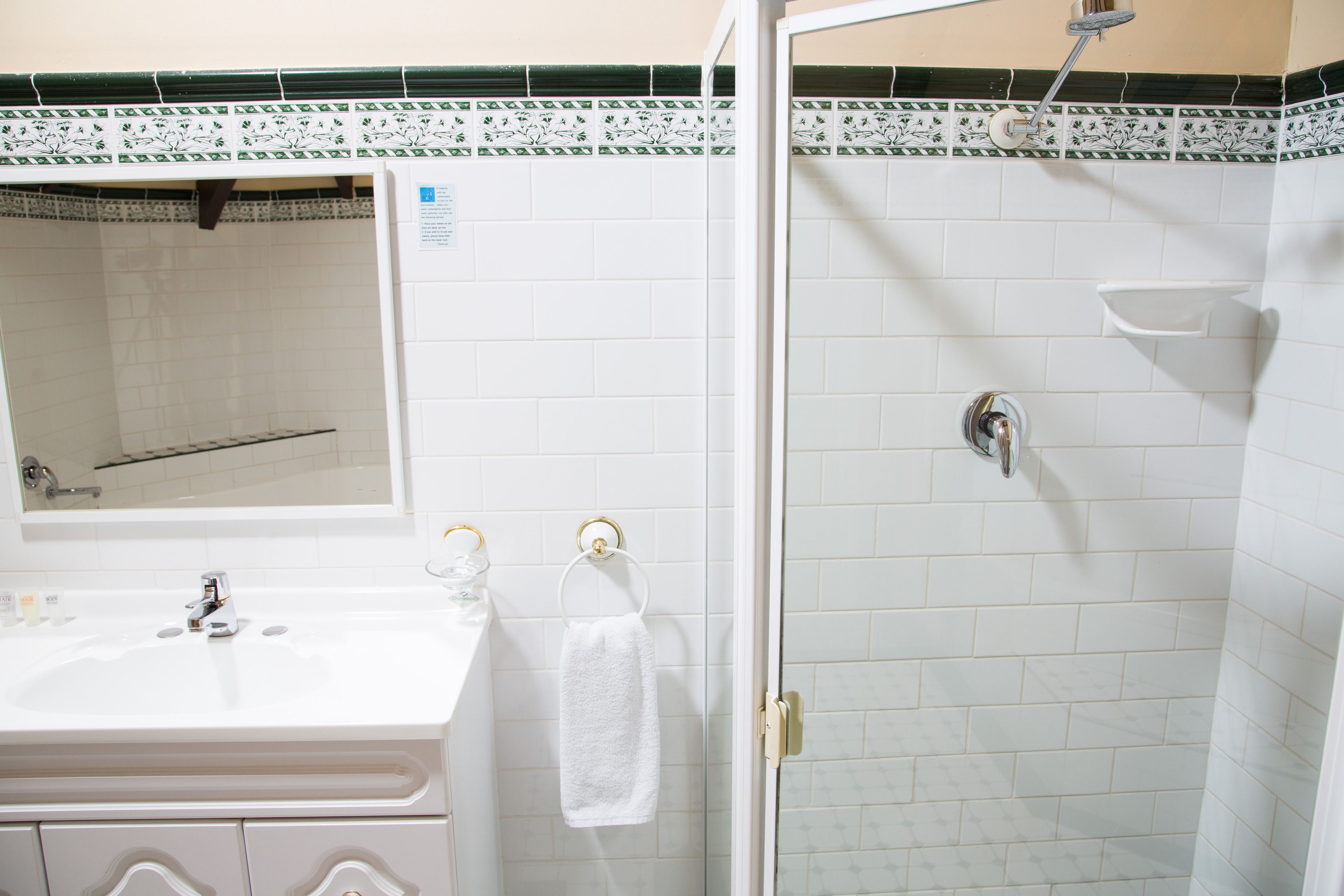 Un bagno con lavandino, specchio e doccia, tutto in bianco.