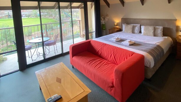 Un dormitorio con una cama grande, un sofá rojo, una mesa de madera y un balcón con mobiliario exterior.