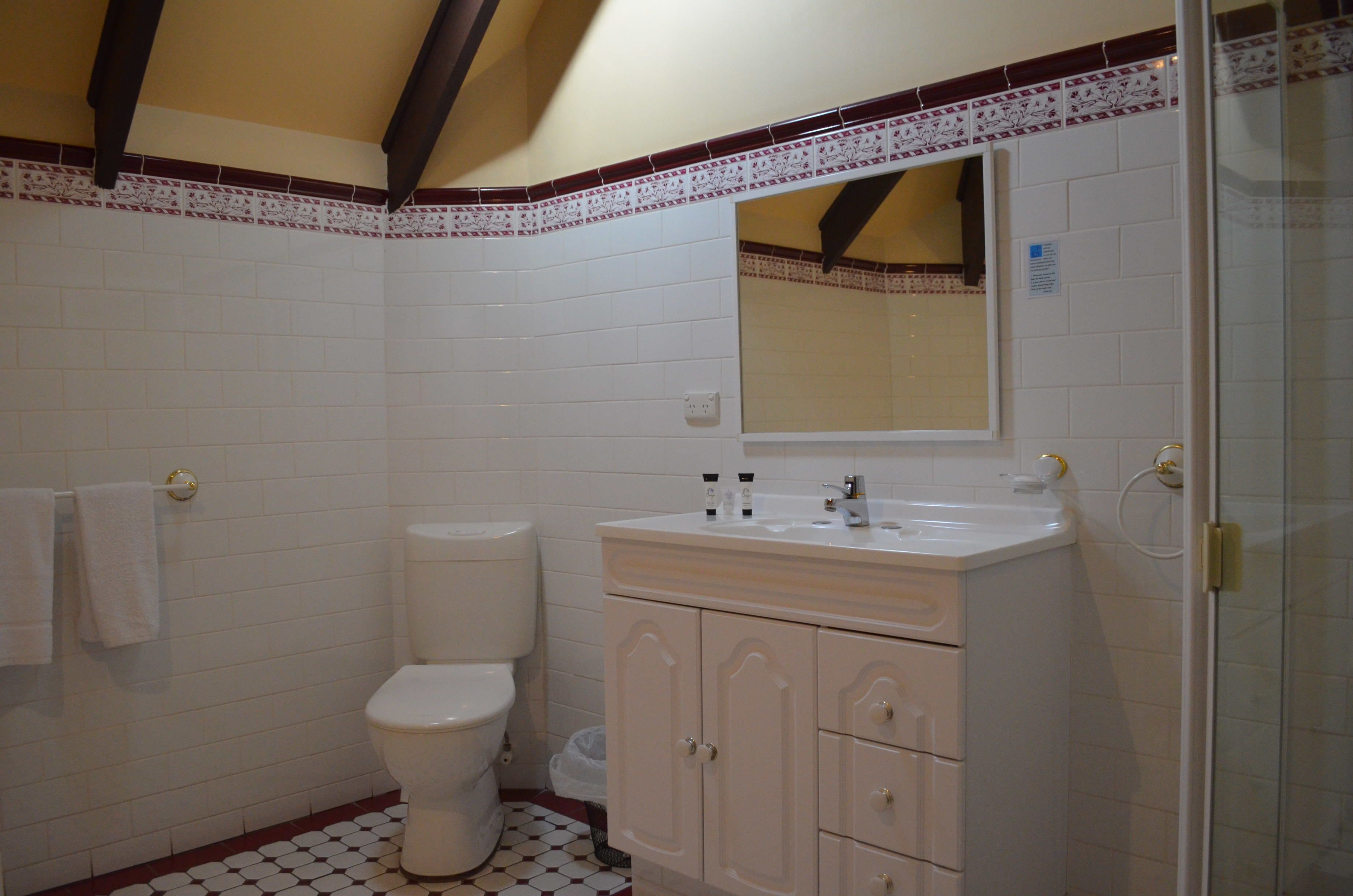 A bathroom with white tiles, a toilet, a sink with cabinets, and a shower area.
