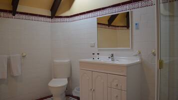 A bathroom with white tiles, a toilet, a sink with cabinets, and a shower area.
