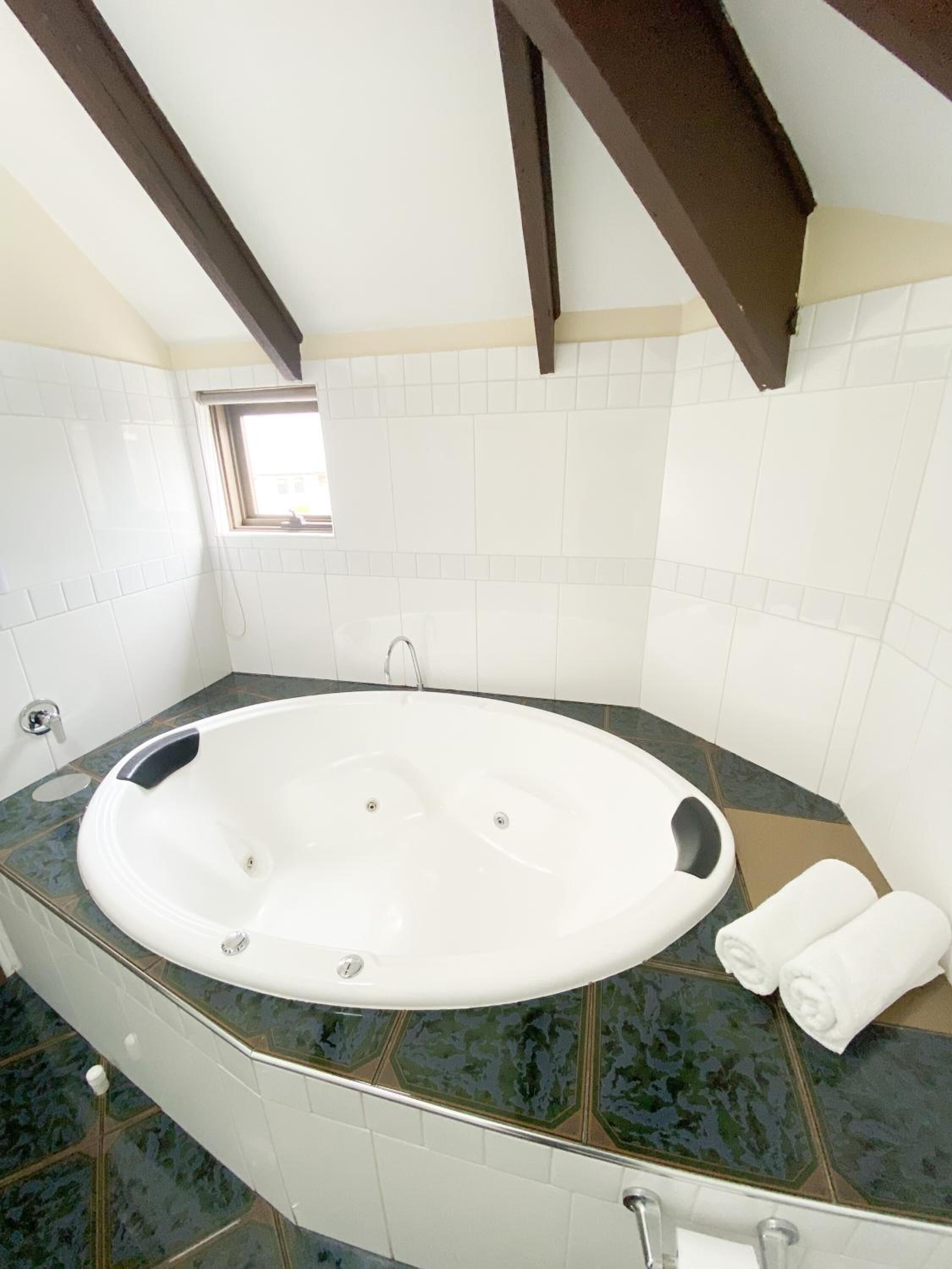 A large oval bathtub with a marble countertop, a small window, and a towel on the side.