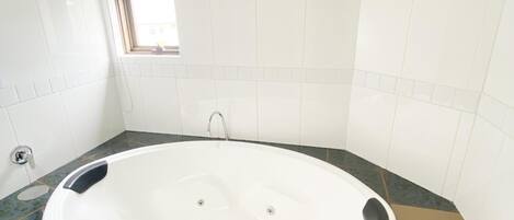 A large oval bathtub with a marble countertop, a small window, and a towel on the side.