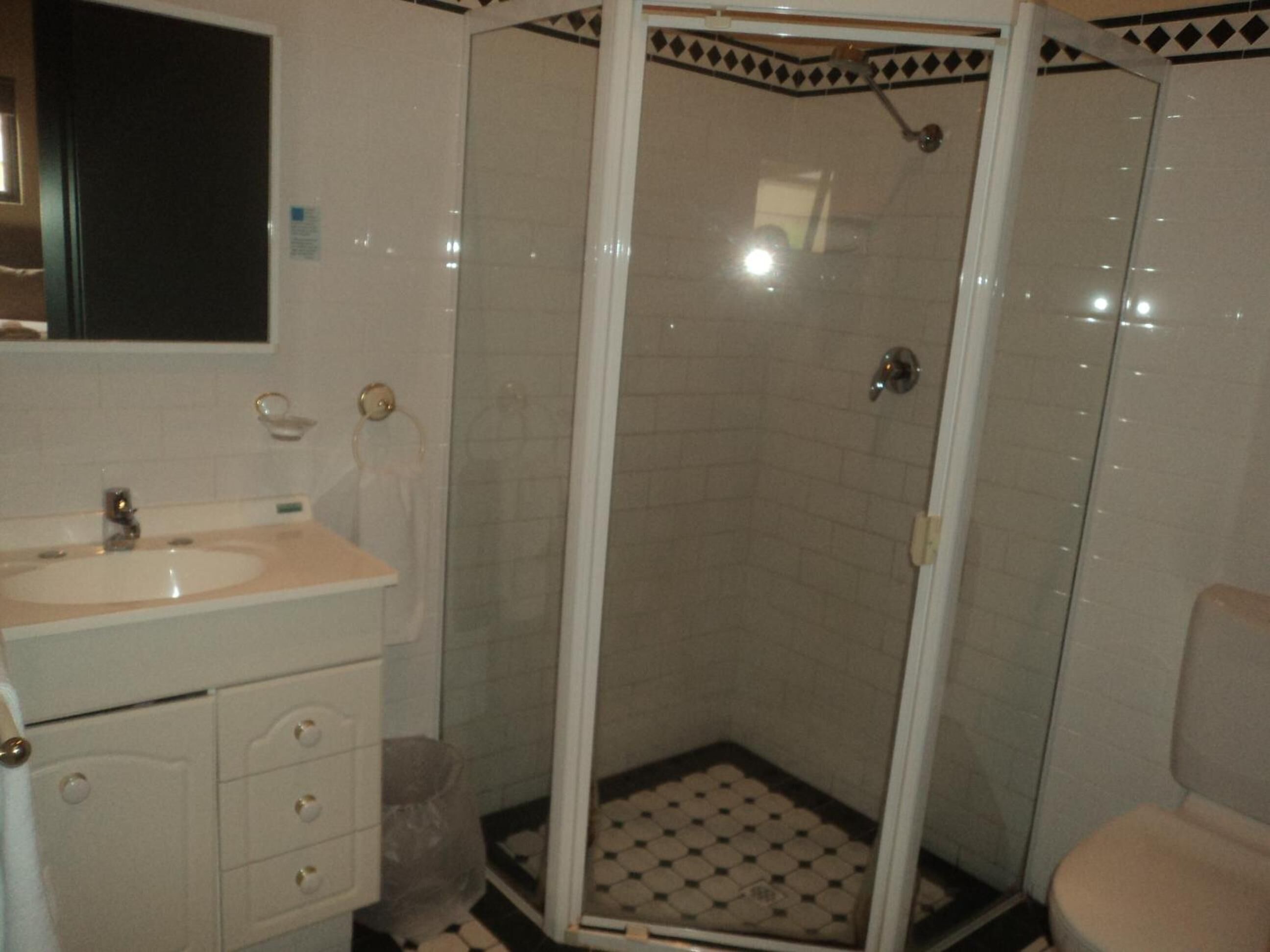 Un baño con lavamanos, espejo y ducha con piso de azulejos.