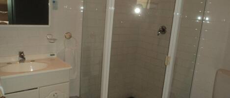 Un baño con lavamanos, espejo y ducha con piso de azulejos.