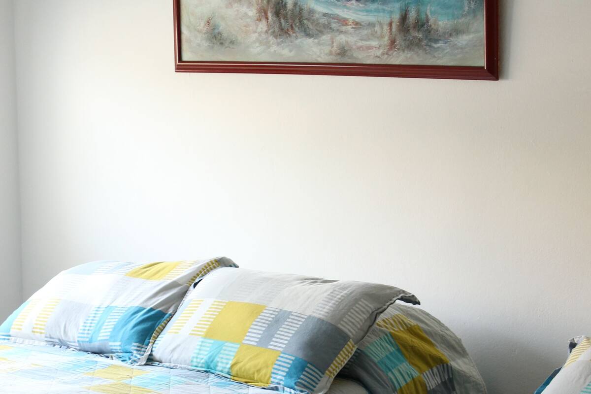 Une chambre à coucher avec deux lits, chacun recouvert d’une courtepointe matelassée et agrémenté d’oreillers. Un tableau encadré est accroché au mur, au-dessus des lits.