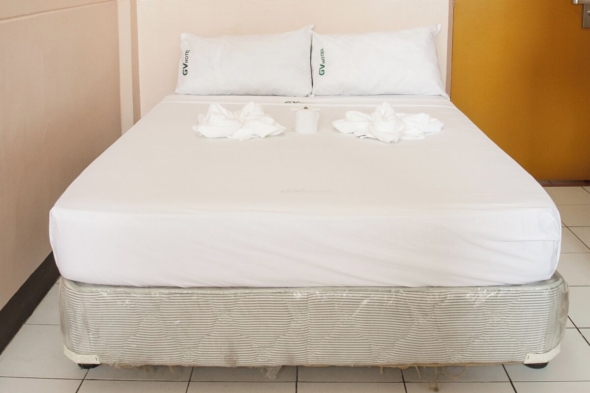 A neatly made bed with two pillows, a wooden door with a notice, and a tiled floor.