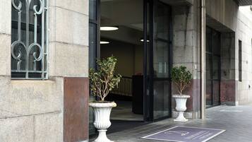 A building entrance with a stone facade, metal window bars, and two potted plants.