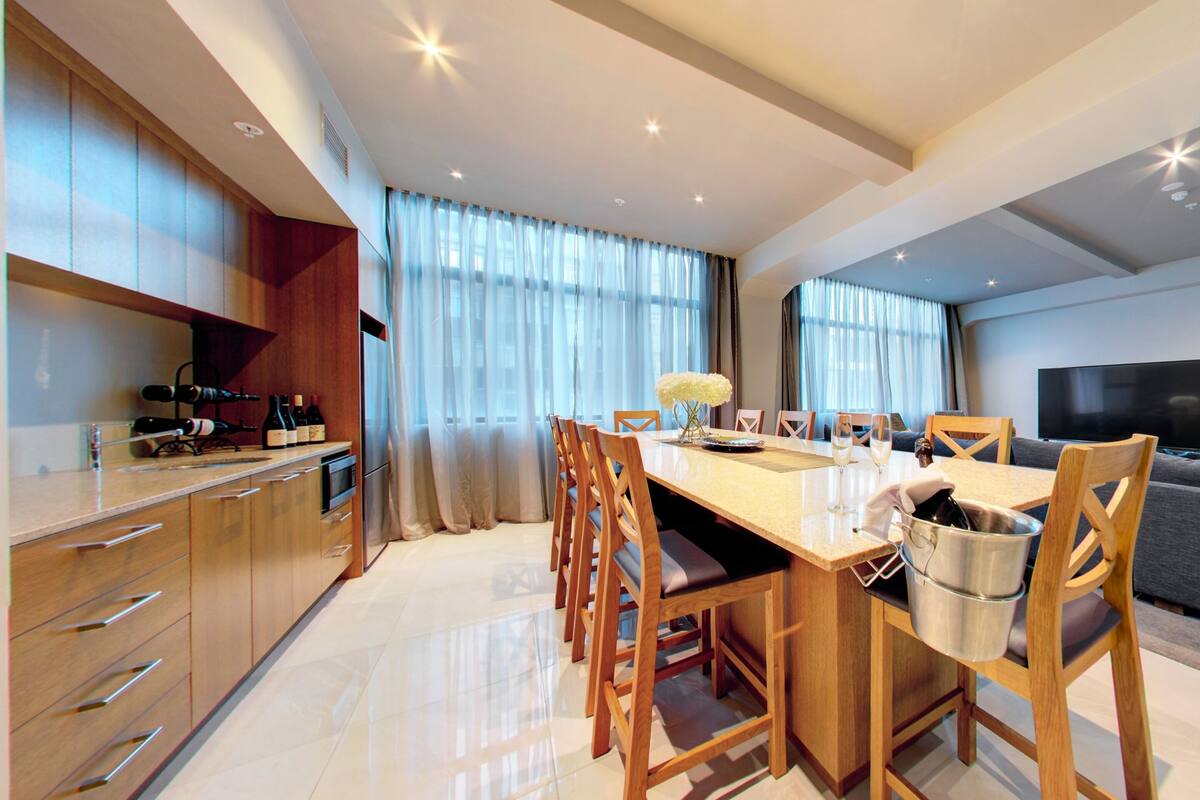 A modern kitchen with wooden cabinets, a dining table with chairs, a built-in oven, and a TV in the living area.