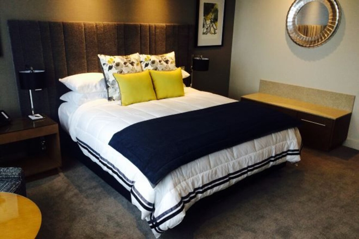 A hotel room with a large bed, a bedside table, a round mirror, and a small round table.