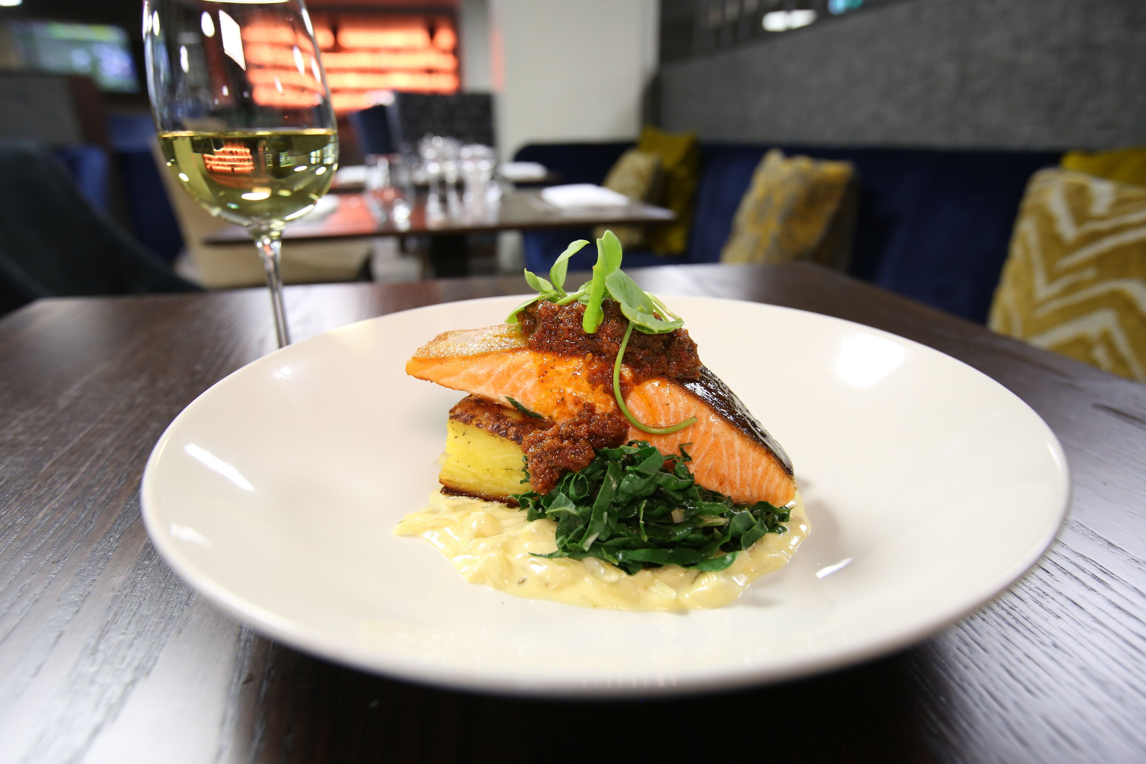 A plate of food with salmon, potatoes, and greens on a white plate.