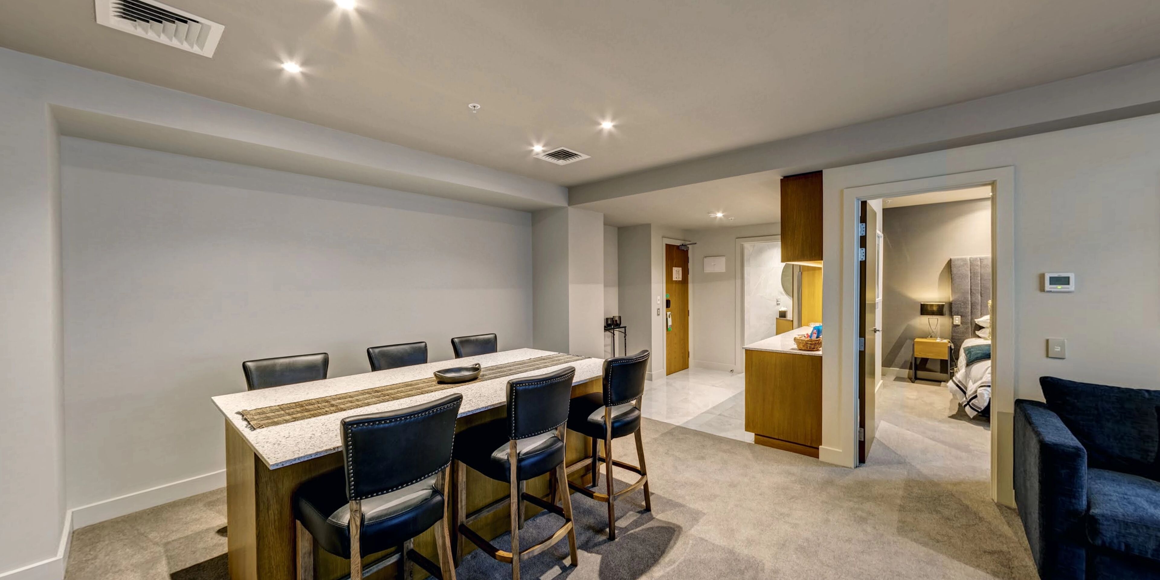 A hotel room with a dining area featuring a table and chairs, a kitchenette, a bathroom, and a living area with a sofa.