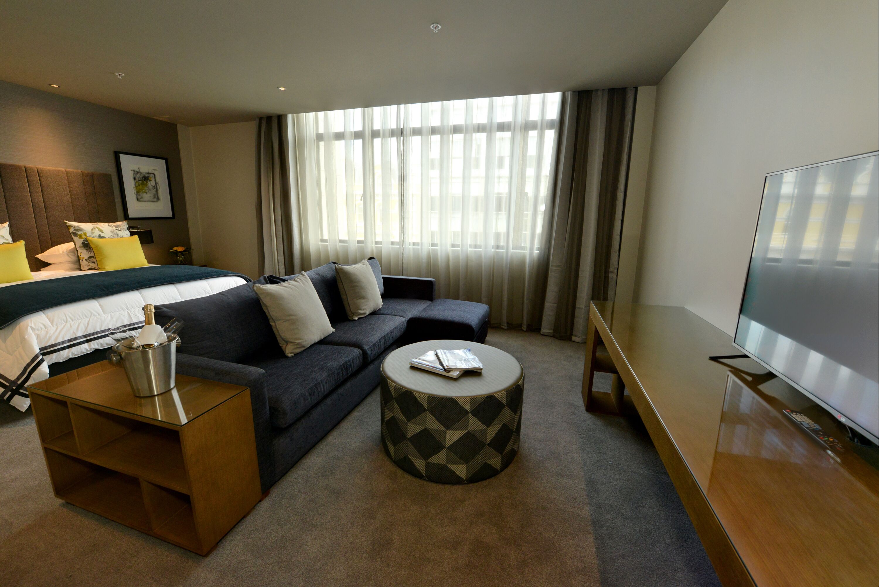 A modern hotel room with a bed, sofa, TV, and a small coffee table.