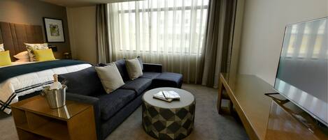 Une chambre d’hôtel moderne équipée d’un lit, d’un canapé, d’une télévision et d’une petite table basse.