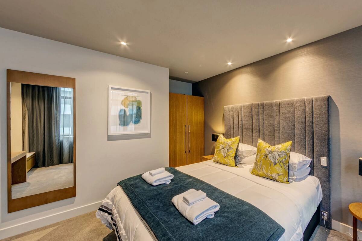 A modern hotel room with a large bed, a mirror, a wardrobe, and a shower area.