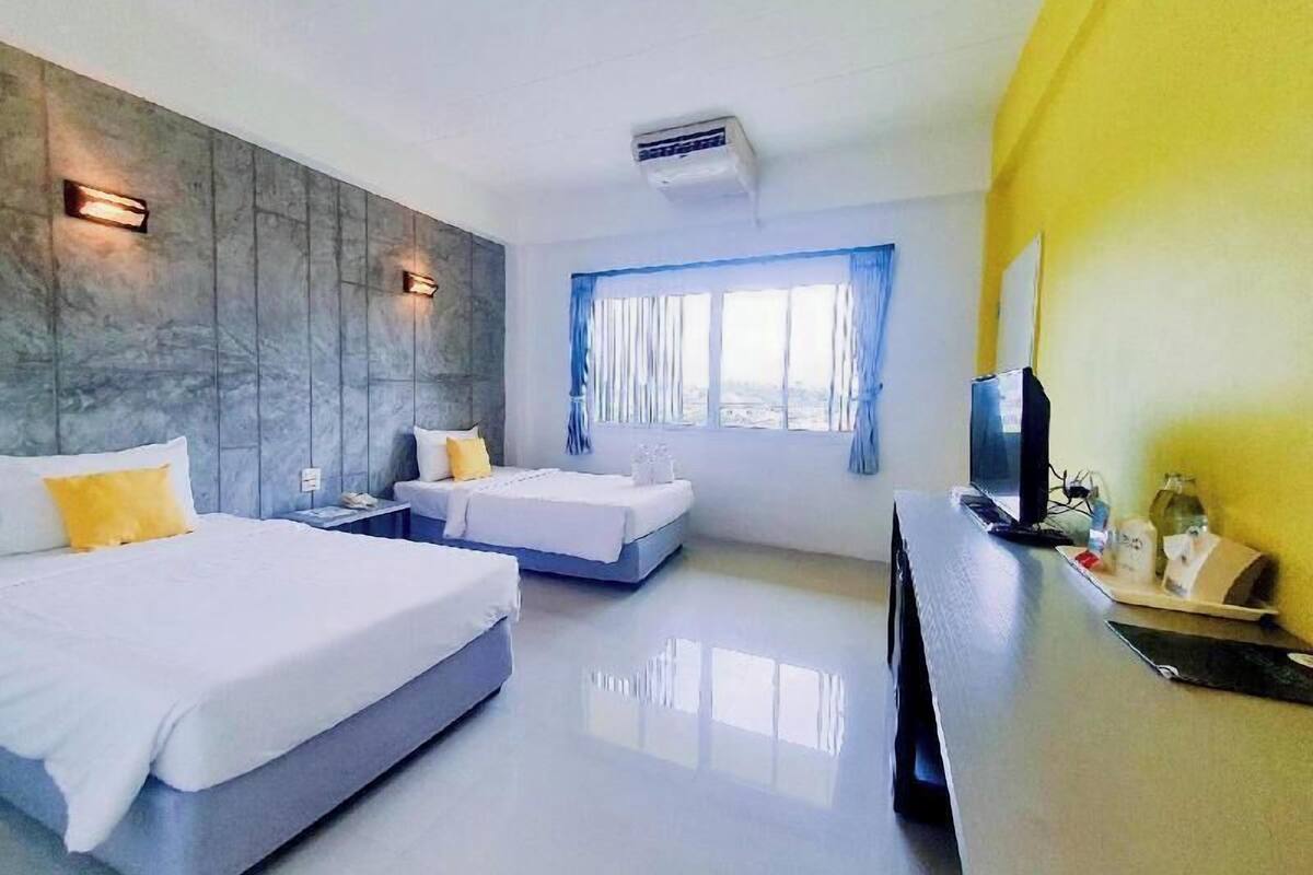 A hotel room with two beds, a desk, a TV, and a window with curtains.