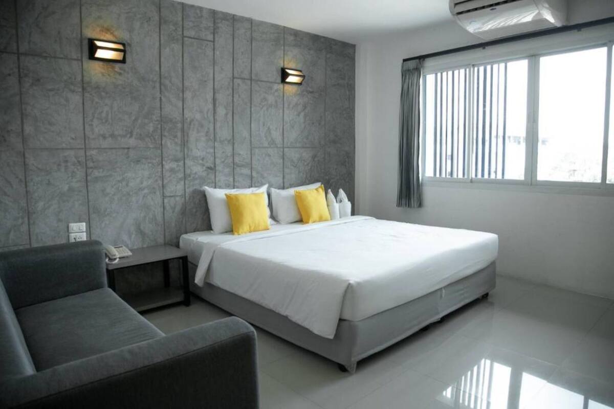 A modern hotel room with a large bed, a sofa, and two wall-mounted lights.