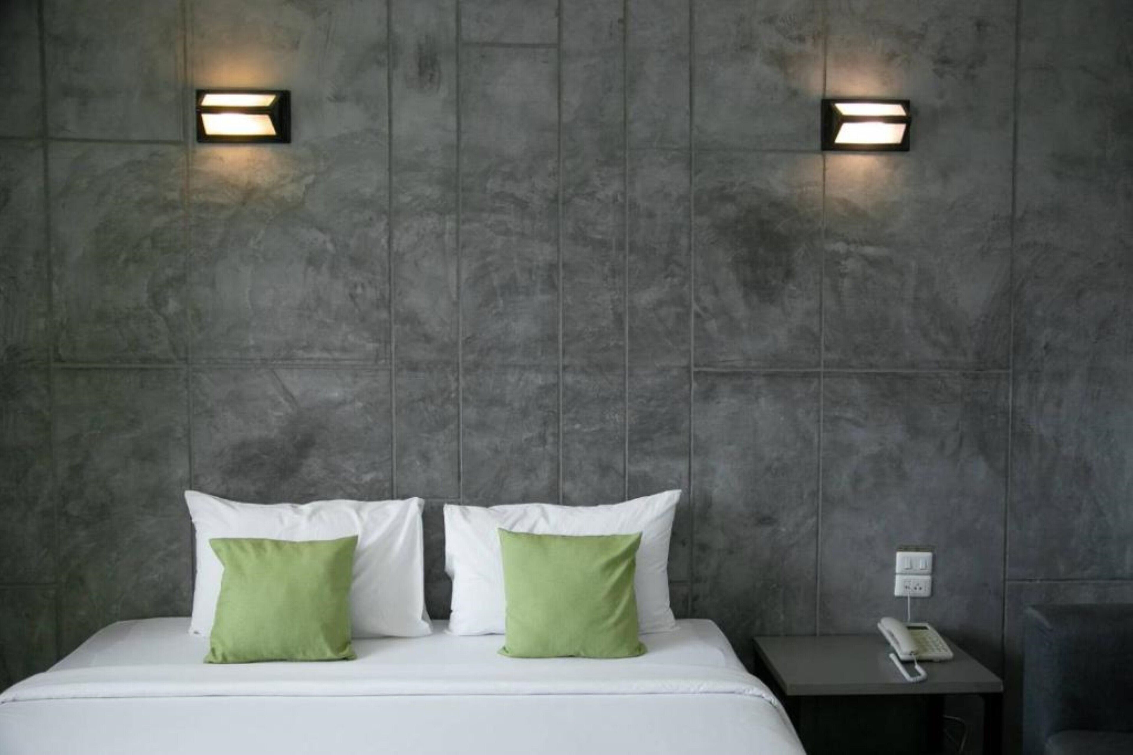 Une chambre d’hôtel avec un grand lit, deux oreillers, une table de chevet avec un téléphone et deux lampes fixées au mur.