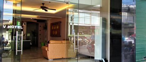 A hotel lobby with a sofa, a ceiling fan, and a reception desk.