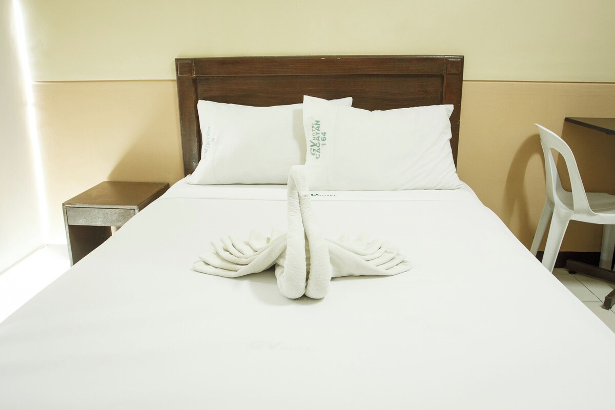 Una cama impecablemente hecha con sábanas blancas y una toalla doblada en forma de lazo.