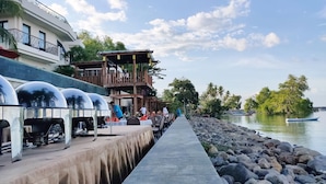 A waterfront restaurant with outdoor seating, a covered area, and a view of the water. - Capa Maumere (Maumere)