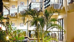 A multi-story hotel with balconies, air conditioning units, and a garden area with a paved walkway. - Capa Maumere (Maumere)