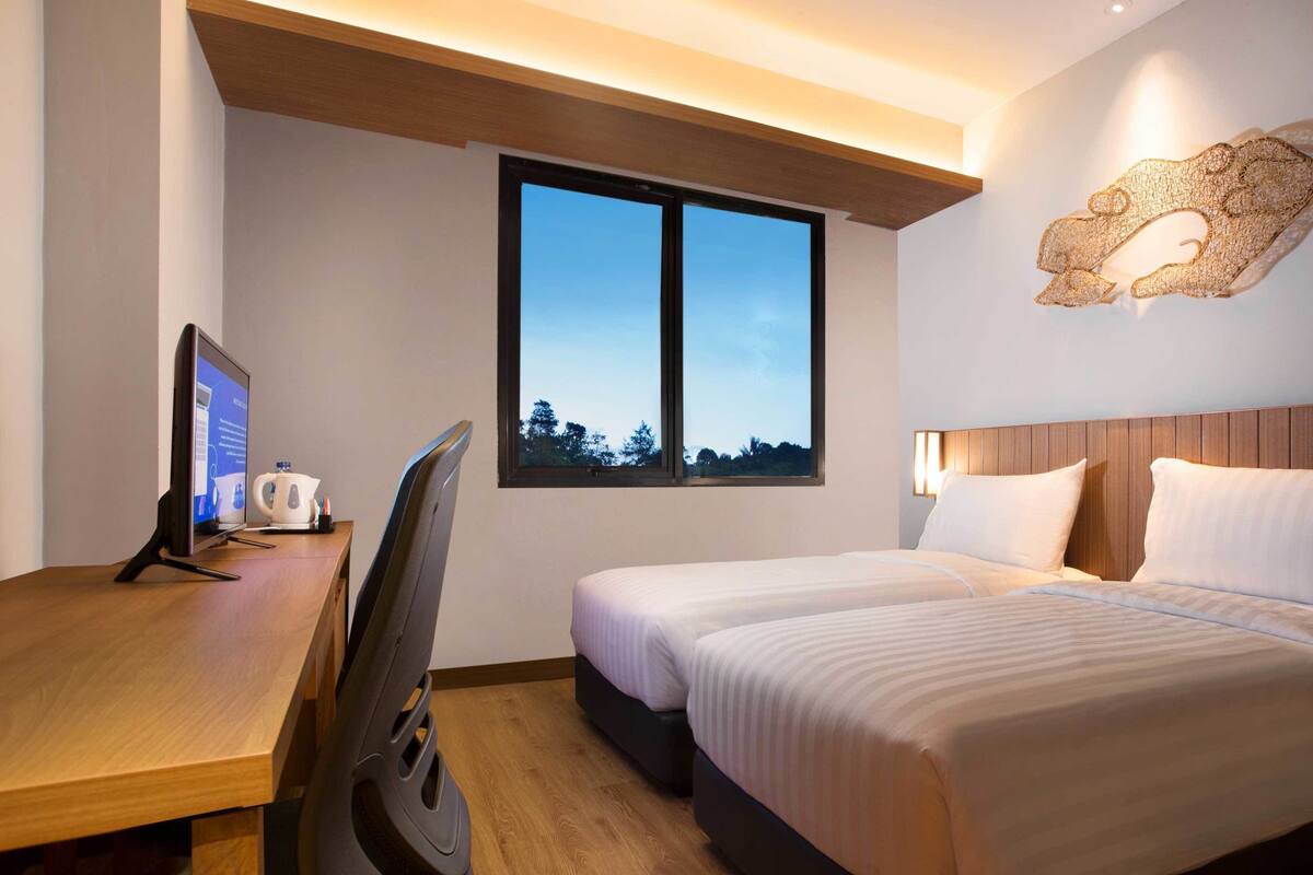 Habitación de hotel con escritorio, dos camas, un ventanal grande y una lámpara fijada a la pared.