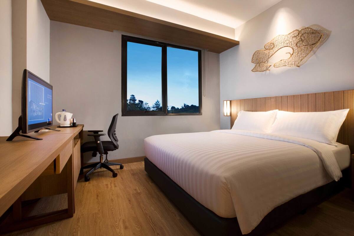 Una habitación de hotel con cama, escritorio, silla y un ventanal grande.