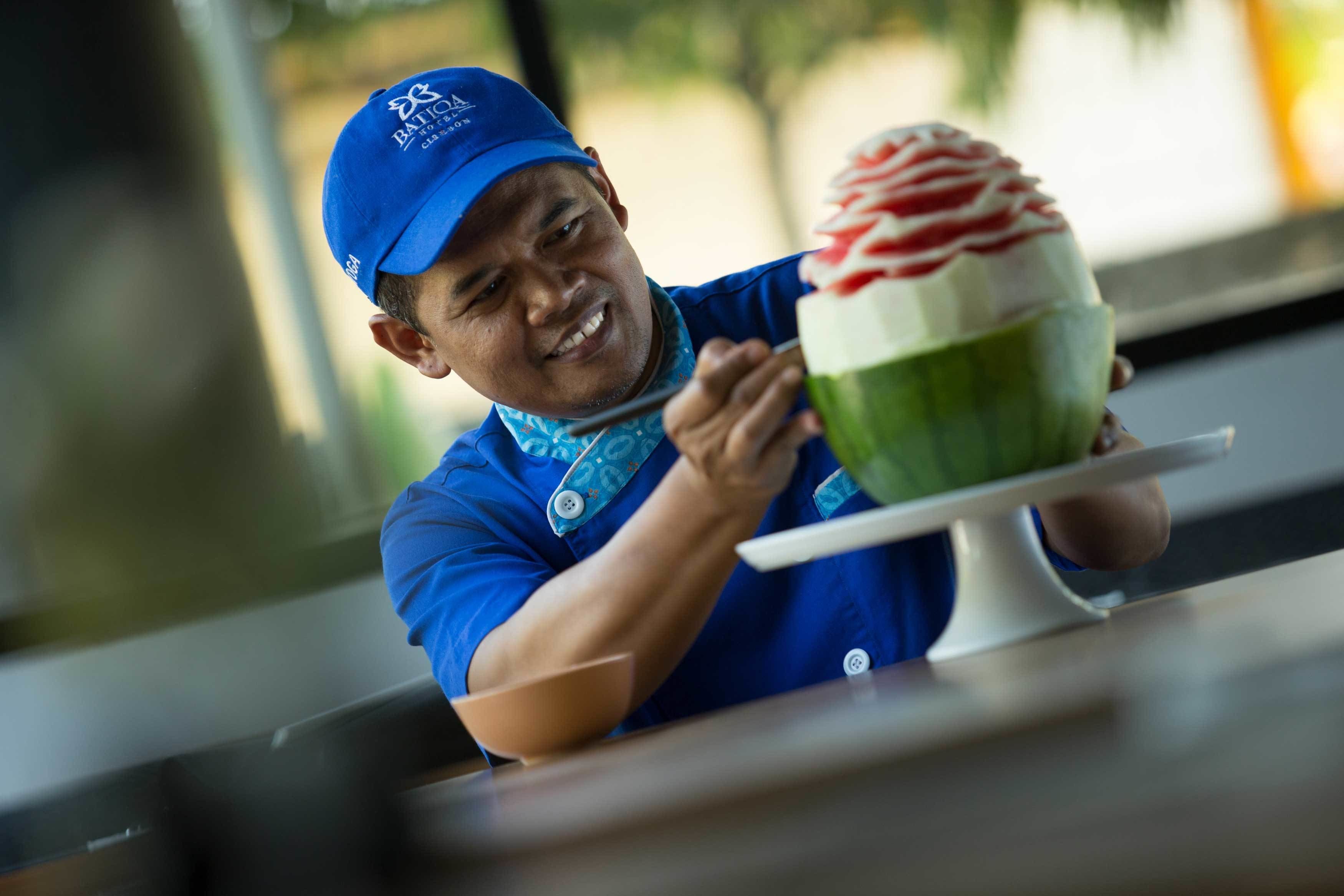 A person in a blue uniform holding a dessert with a white and green base and red toppings.