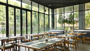 Un restaurant amb taules i caires de fusta, grans finestres i vista a zones verds a l'exterior.