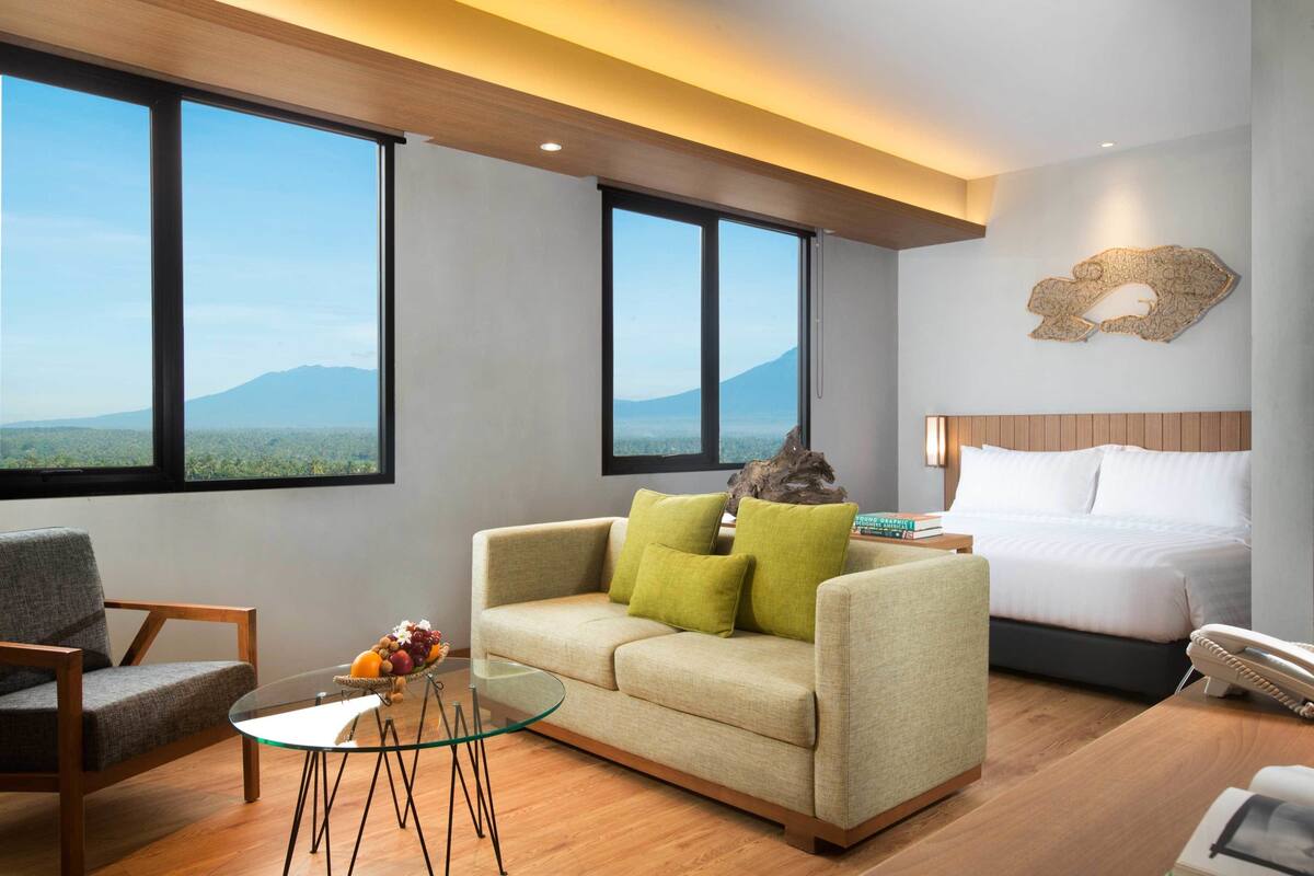 Una habitación de hotel moderna con una cama grande, un sofá, una mesa de centro de vidrio y vistas a la montaña.