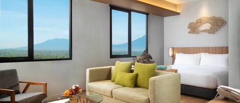 Una habitación de hotel moderna con una cama grande, un sofá, una mesa de centro de vidrio y vistas a la montaña.