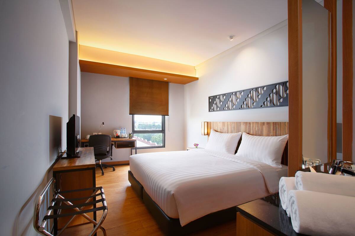 A hotel room with a large bed, a desk with a computer, a chair, and a window with a view.