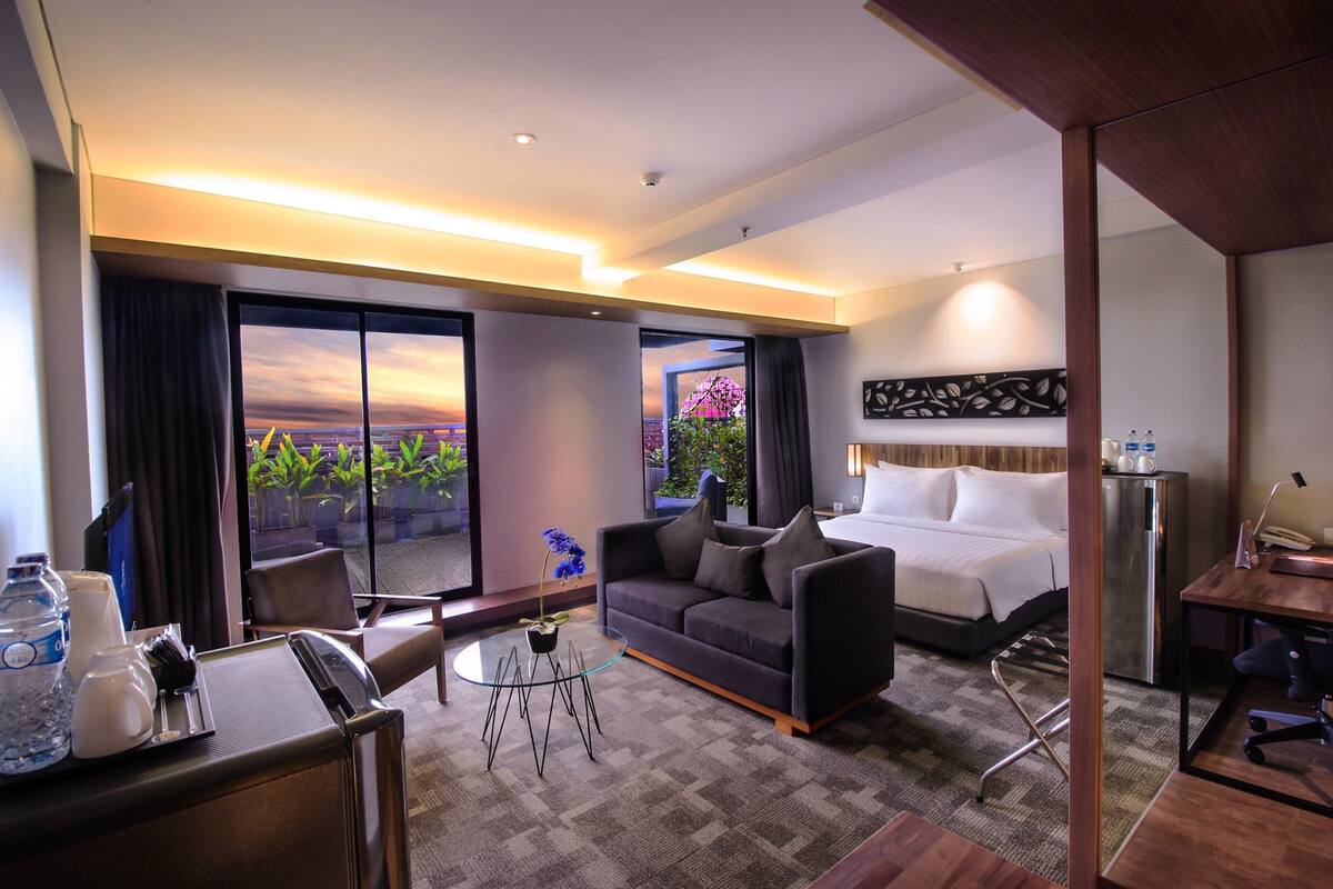A hotel room with a bed, a sofa, a desk, and a view of the outdoors.