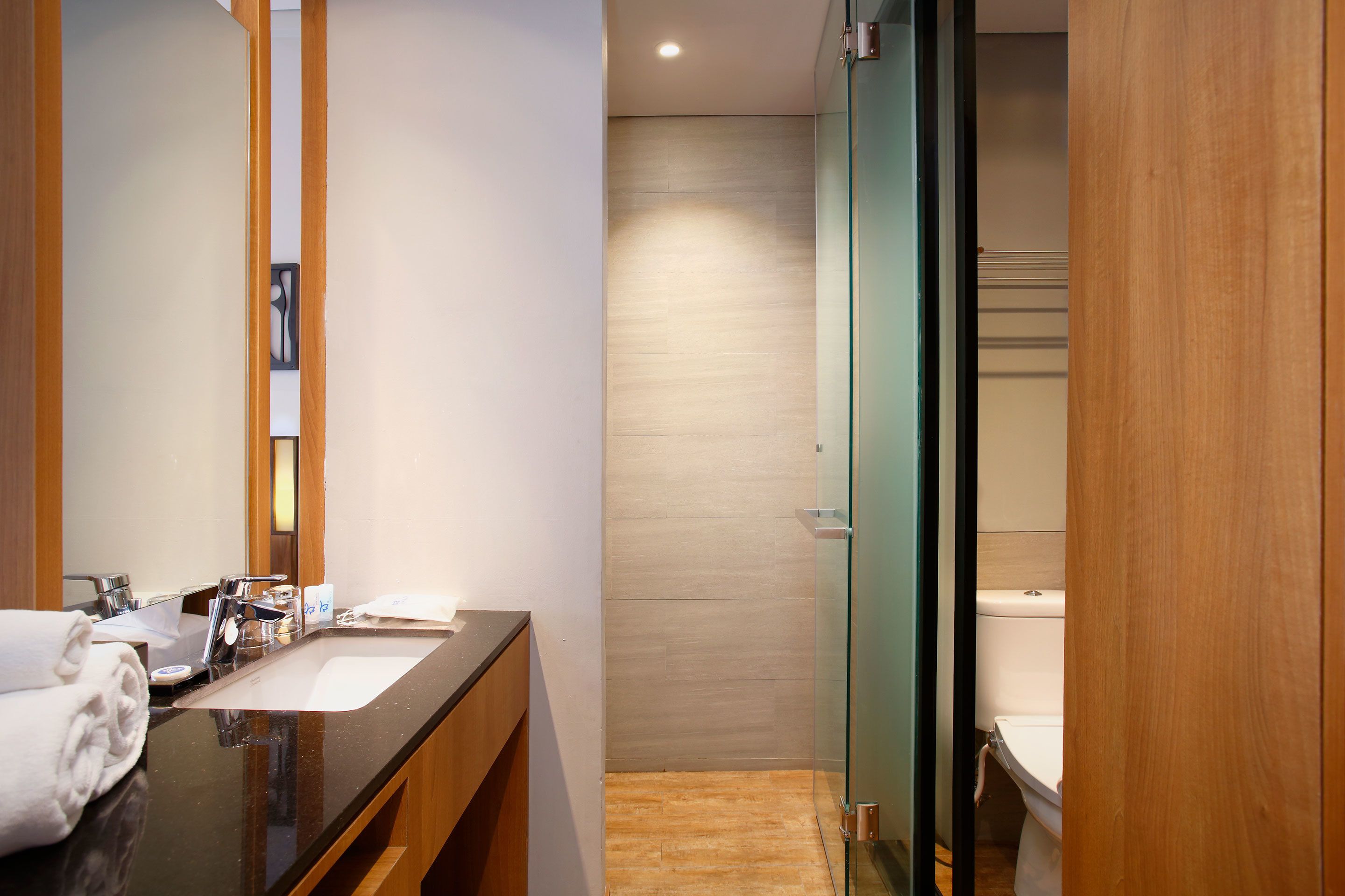 A modern bathroom with a wooden vanity, a glass shower enclosure, and a white toilet.