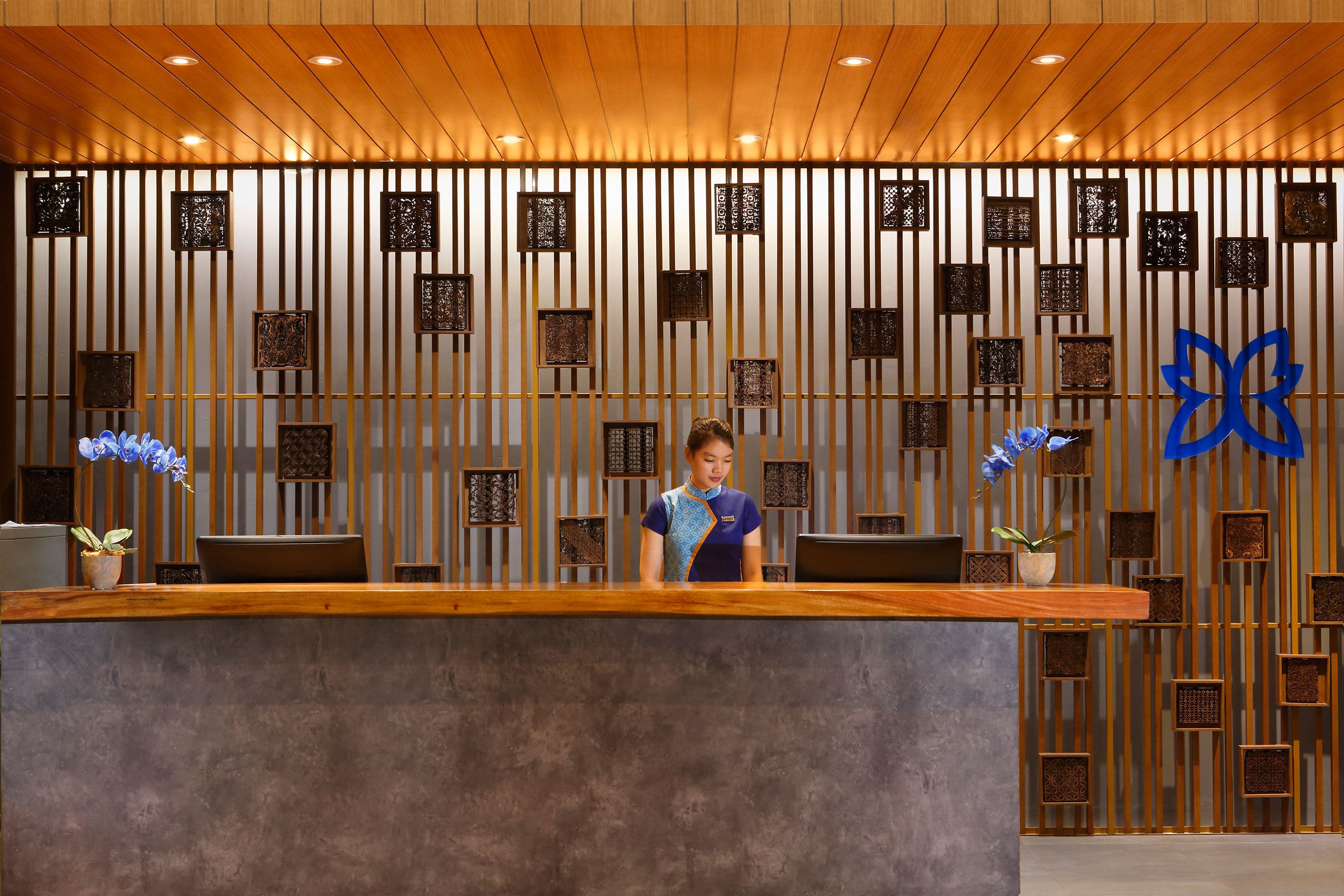 A reception desk with a wooden finish, a receptionist, and decorative elements including vertical panels and a blue logo.