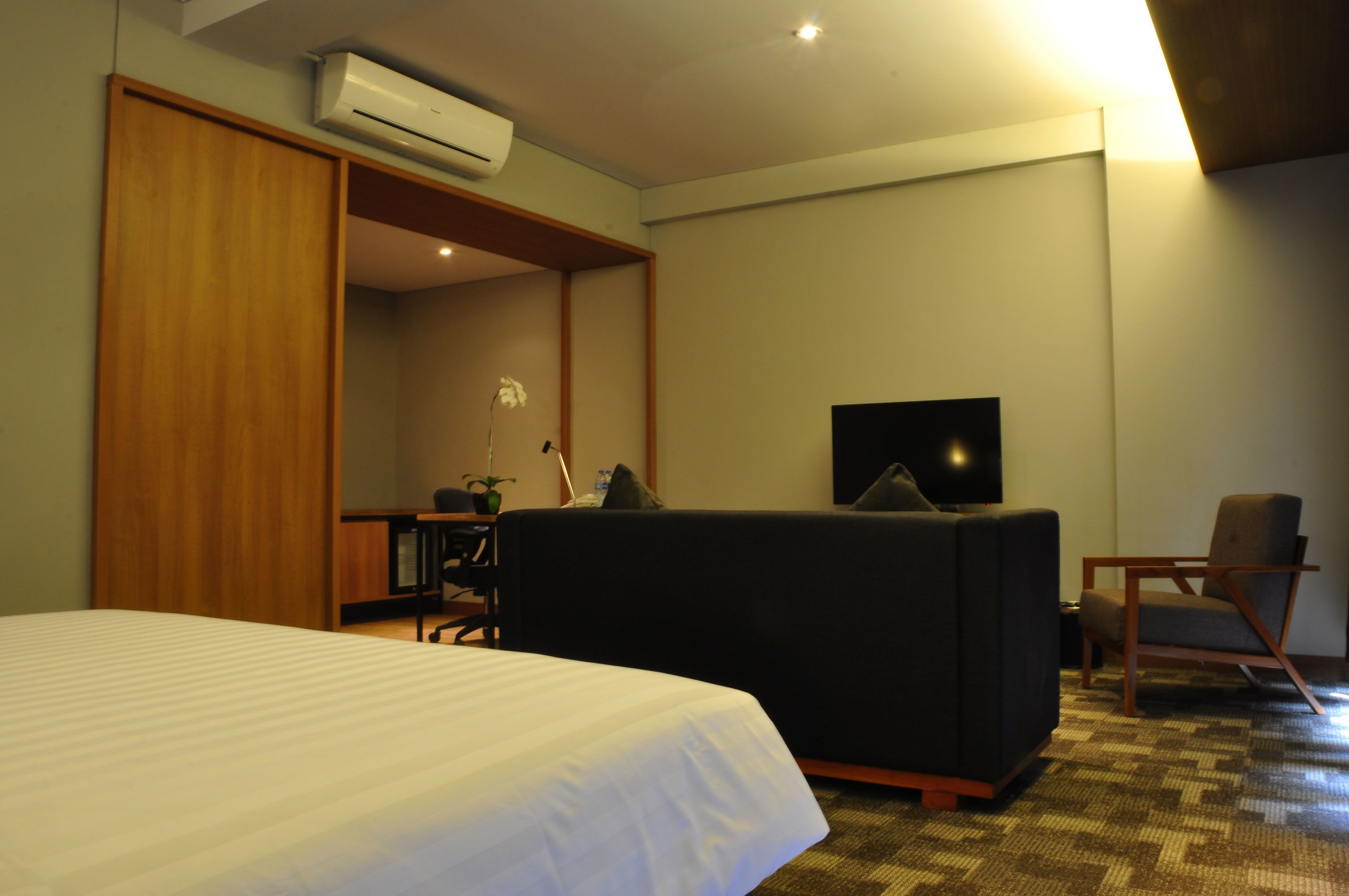 Une chambre d’hôtel équipée d’un lit, d’un canapé, d’une télévision, d’un fauteuil et d’un appareil de climatisation.
