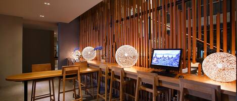 A modern bar area with a long wooden table, several bar stools, and a large screen displaying a scenic view.