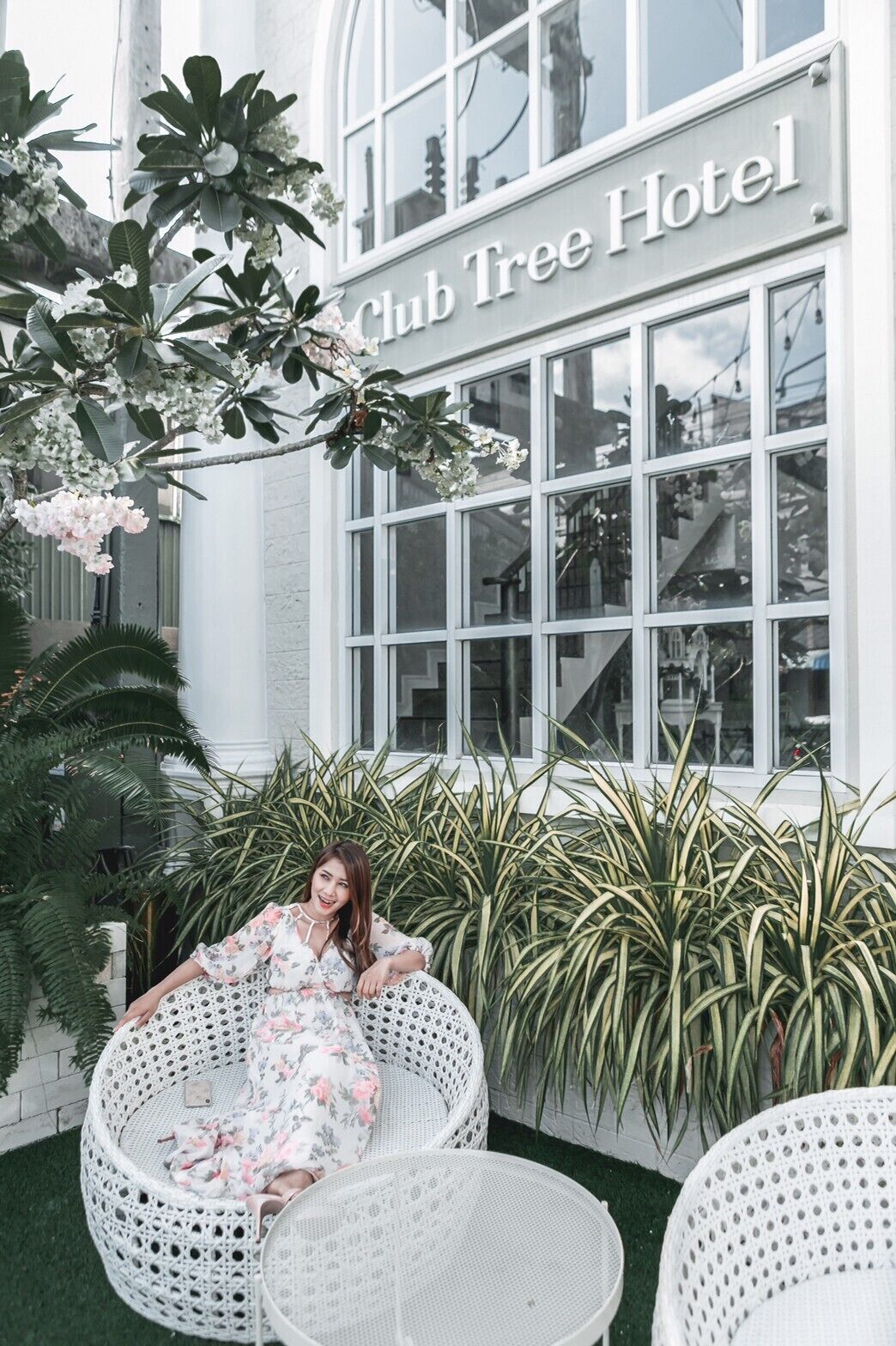 A woman sitting on a wicker chair in front of the Club Tree Hotel.