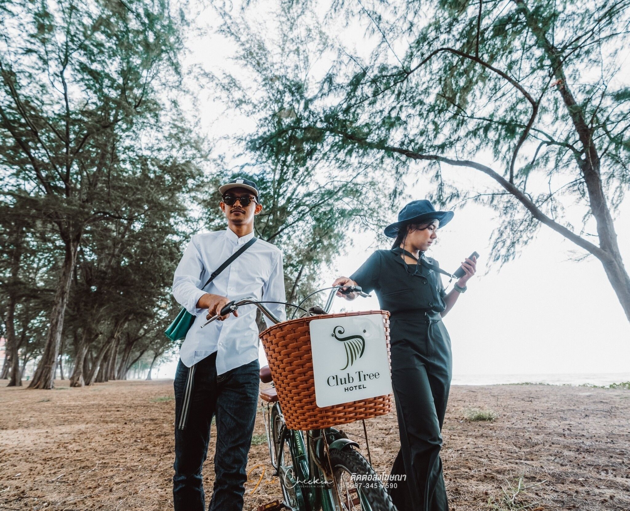 Two people standing next to a bicycle with a basket labeled "Club Tree Hotel".